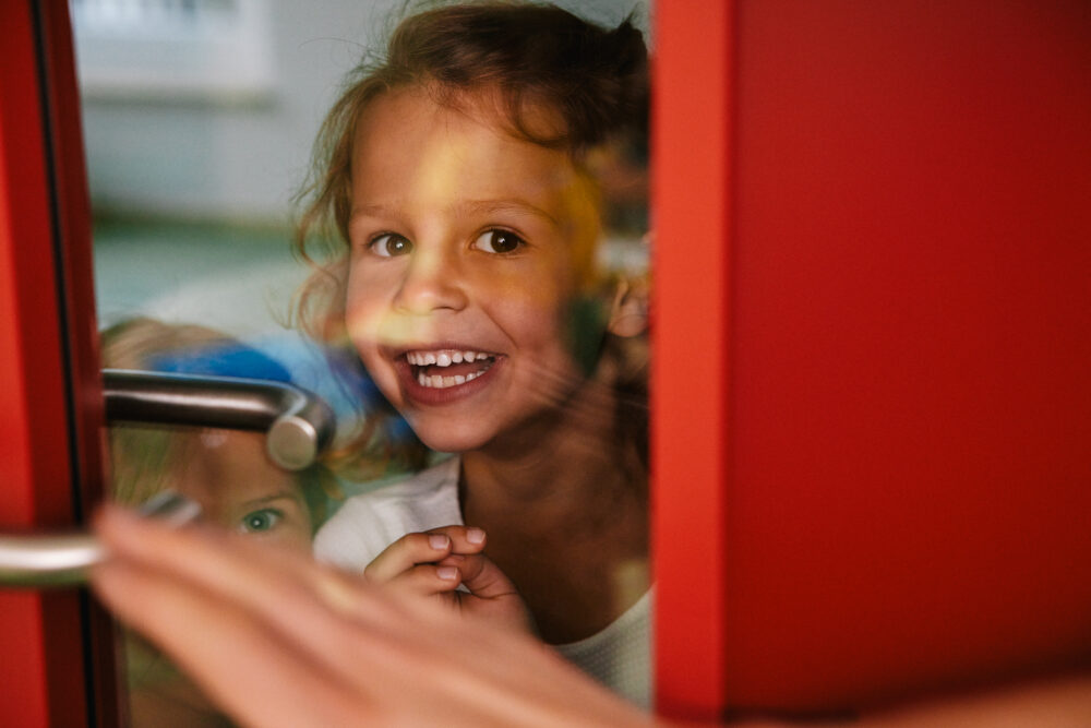 Mädchen versteckt sich hinter einer Tür und lächelt verstohlen in die Kamera