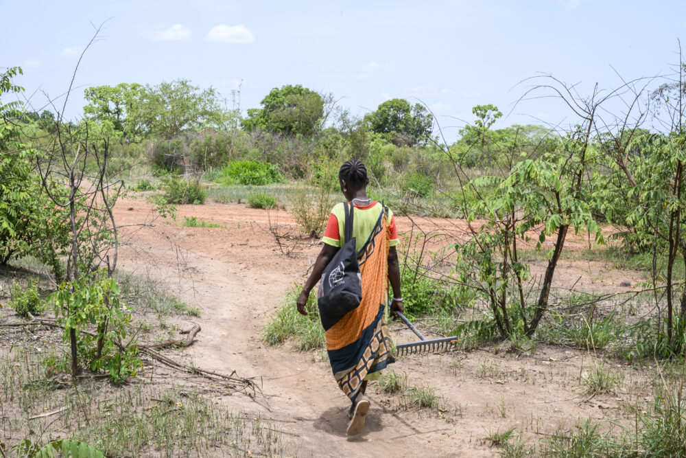 Frau aus Südsudan läuft mit einem Besen in der Hand durch die Savanne