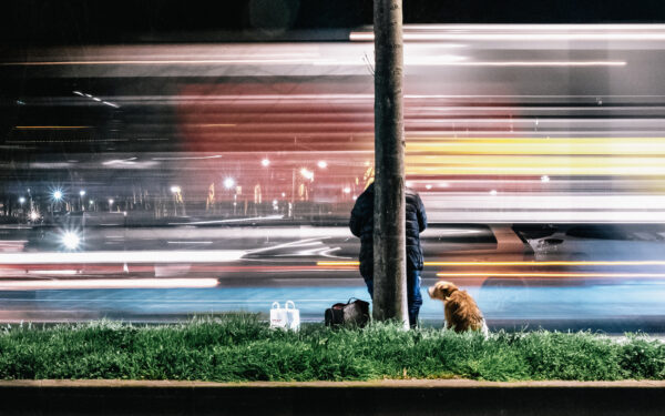 Obdachlose Person steht mit ihrem Hund einsam am Straßenrand