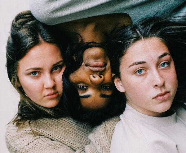 Drei Frauengesichter die liegend auf dem Boden angespannt in die Kamera gucken