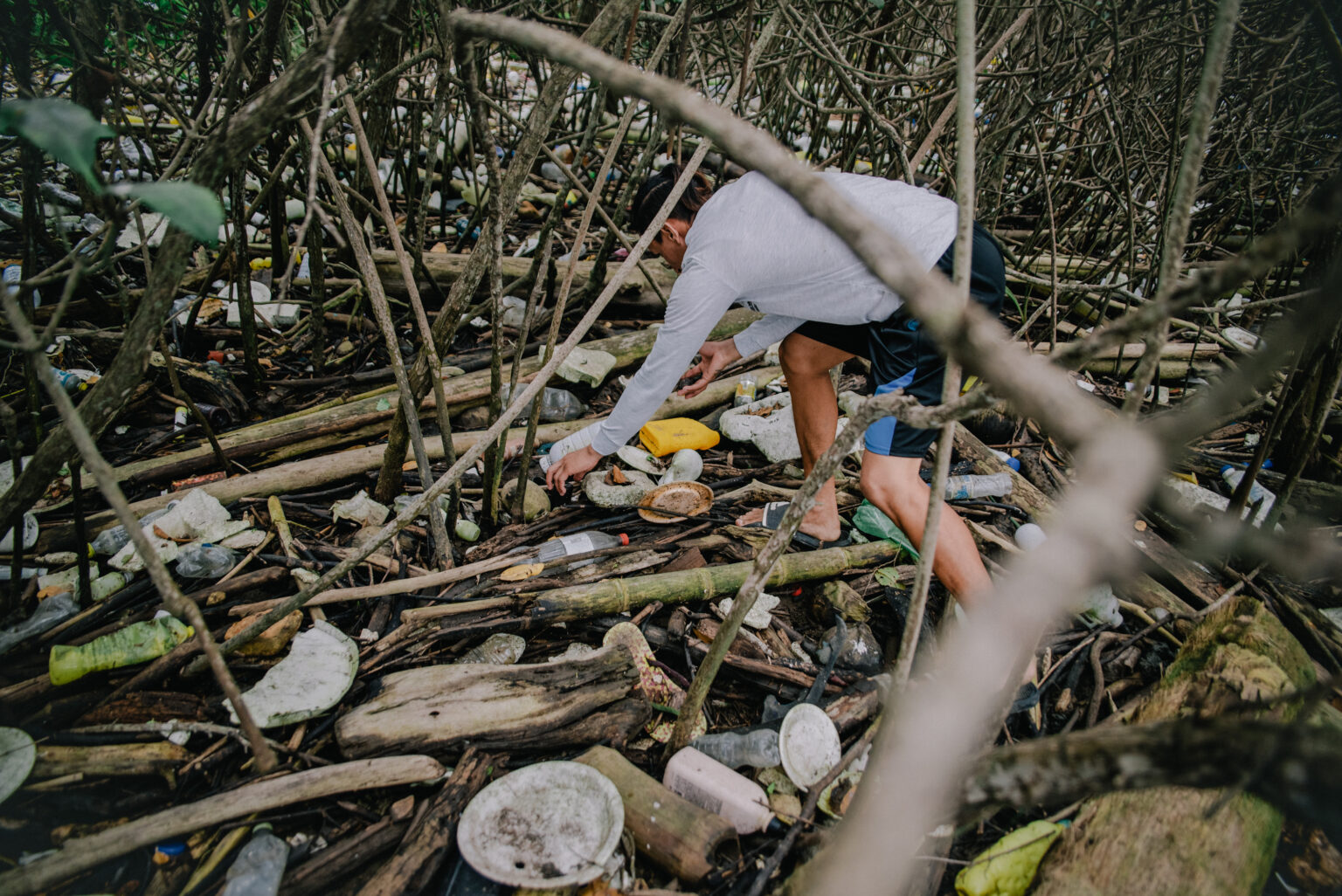 Mann sammelt Müll aus einem kleinen Waldstück, dass mit Ästen übersäht ist