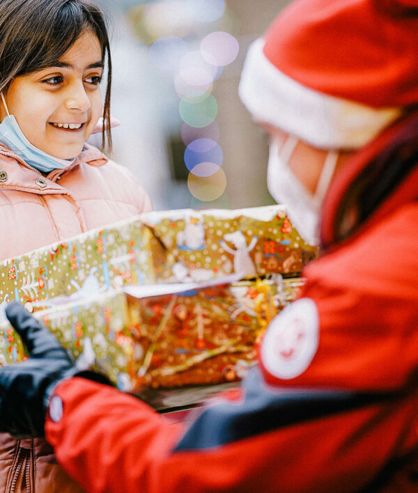 Mitarbeiter der Johanniter ist als Weihnachtsmann verkleidet und überreicht kleinem Mädchen ein Geschenk