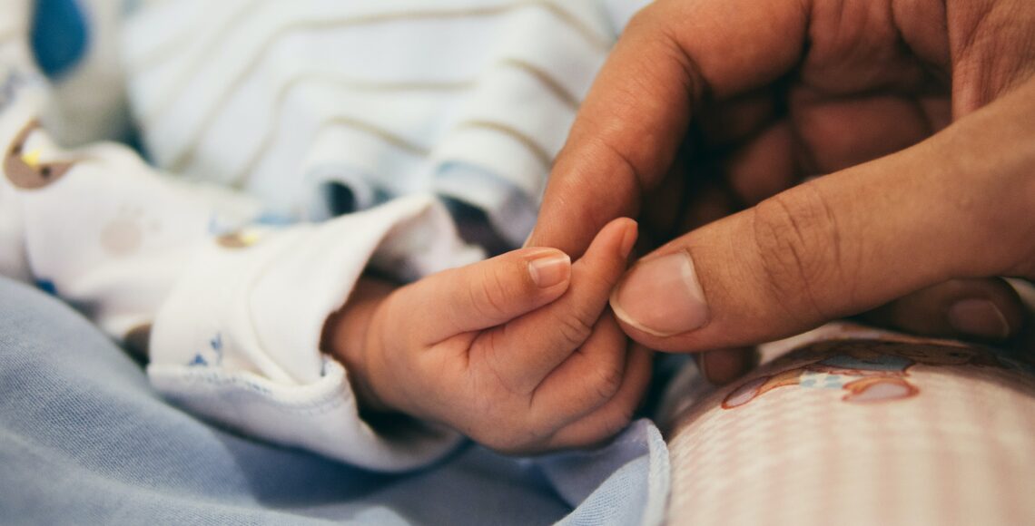 Hand eines Erwachsenen hält die eines Säuglings.