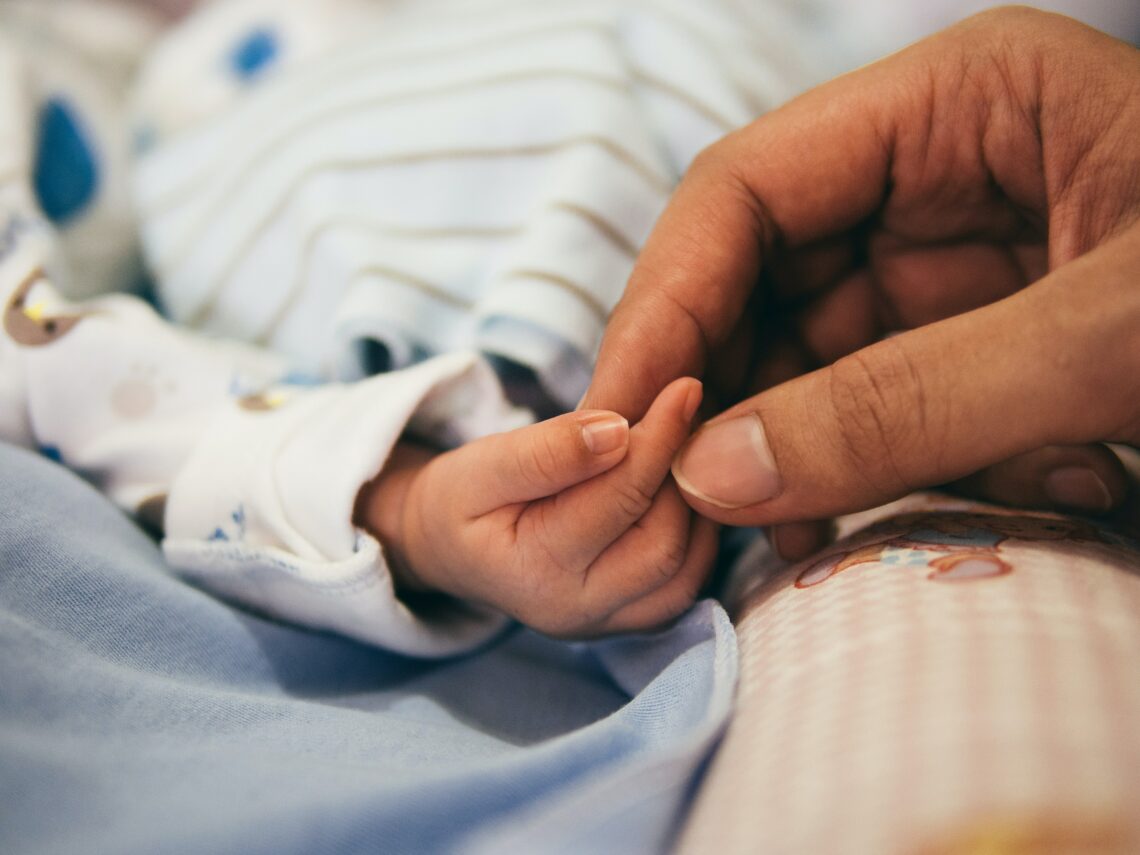 Hand eines Erwachsenen hält die eines Säuglings.
