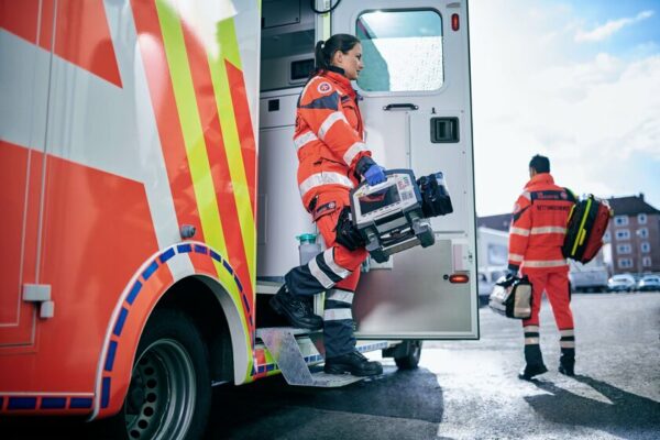 Rettungsassistenten steigen mit einem Defibrilator aus einem Einsatzfahrzeug zum Unfallort