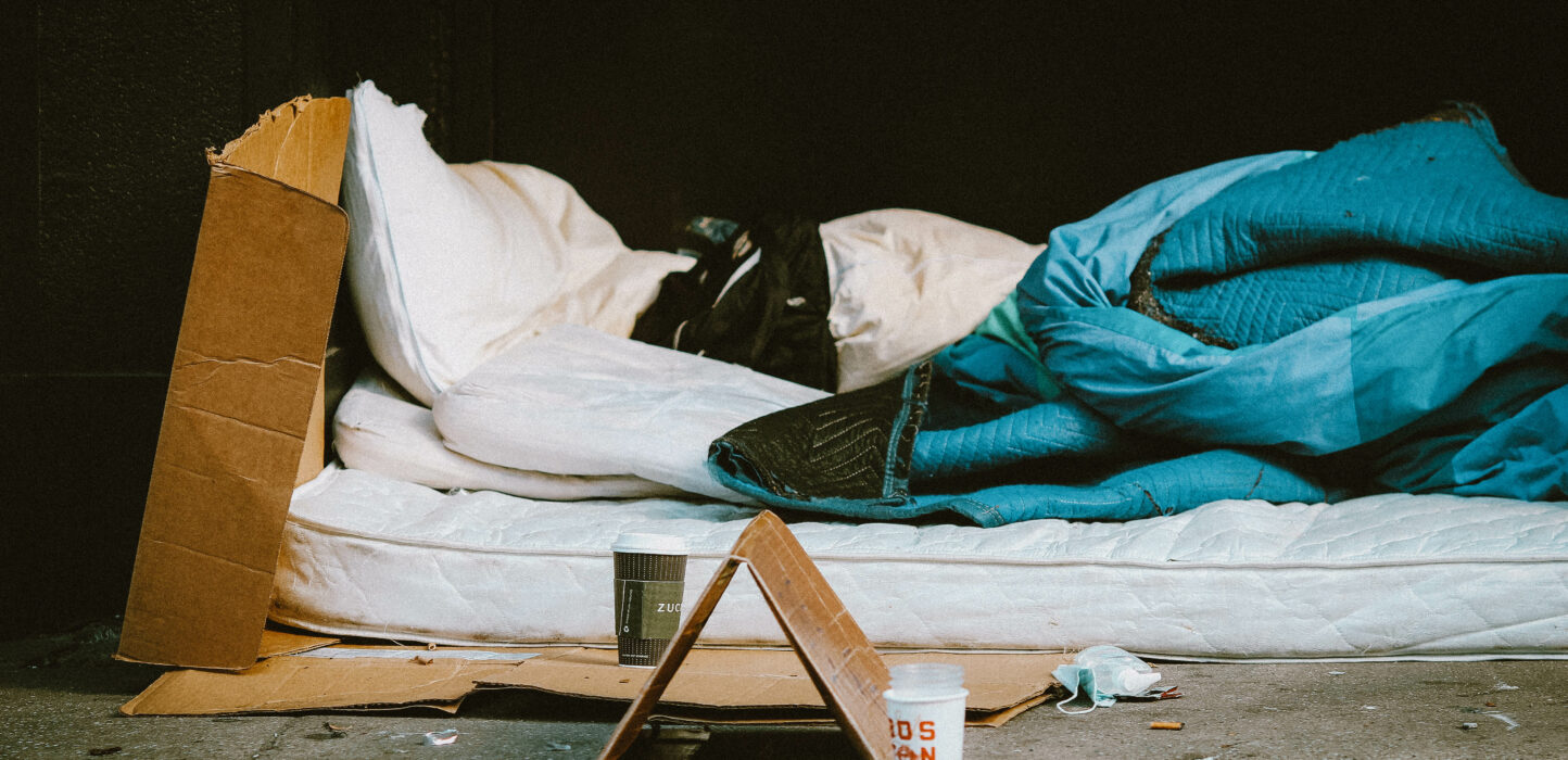 Obdachlose Person schläft auf selbstgemachtem Bett aus Matratzen und Pappe auf der Straße
