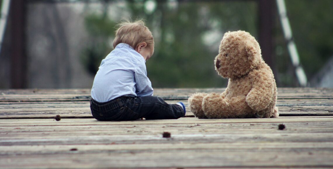 Kleiner Junge sitzt mit einem großen Teddy auf einer Treppe