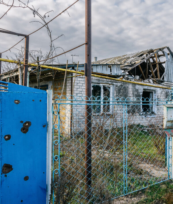 Ein baufälliges und zerstörtes Haus. Links ist eine blaue Wand mit Schusslöchern zu sehen.