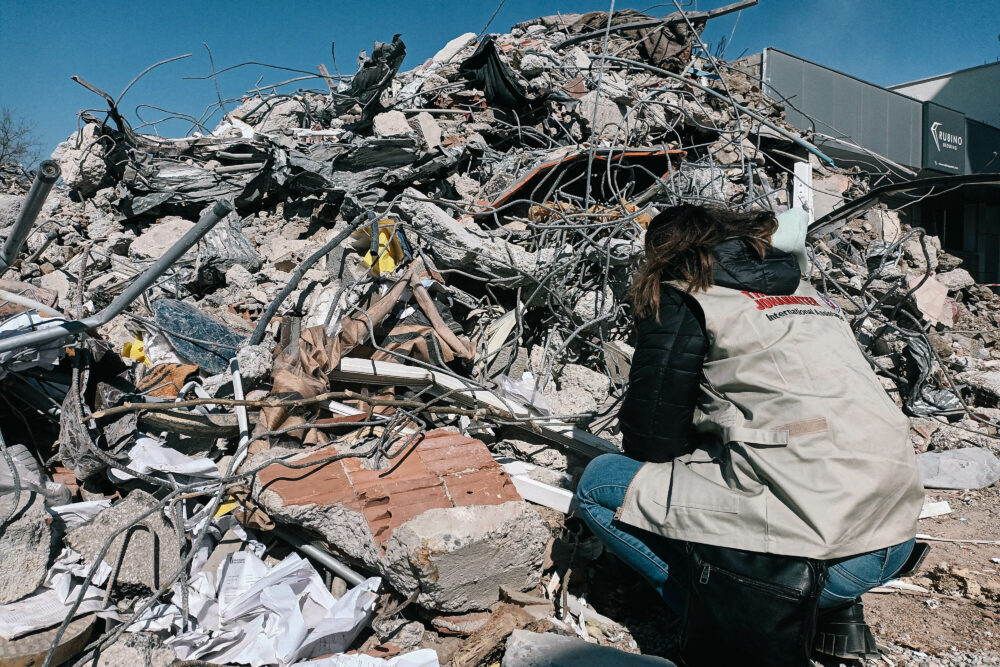 Eine Helferin der Johanniter kniet vor einem Berg aus Trümmern.