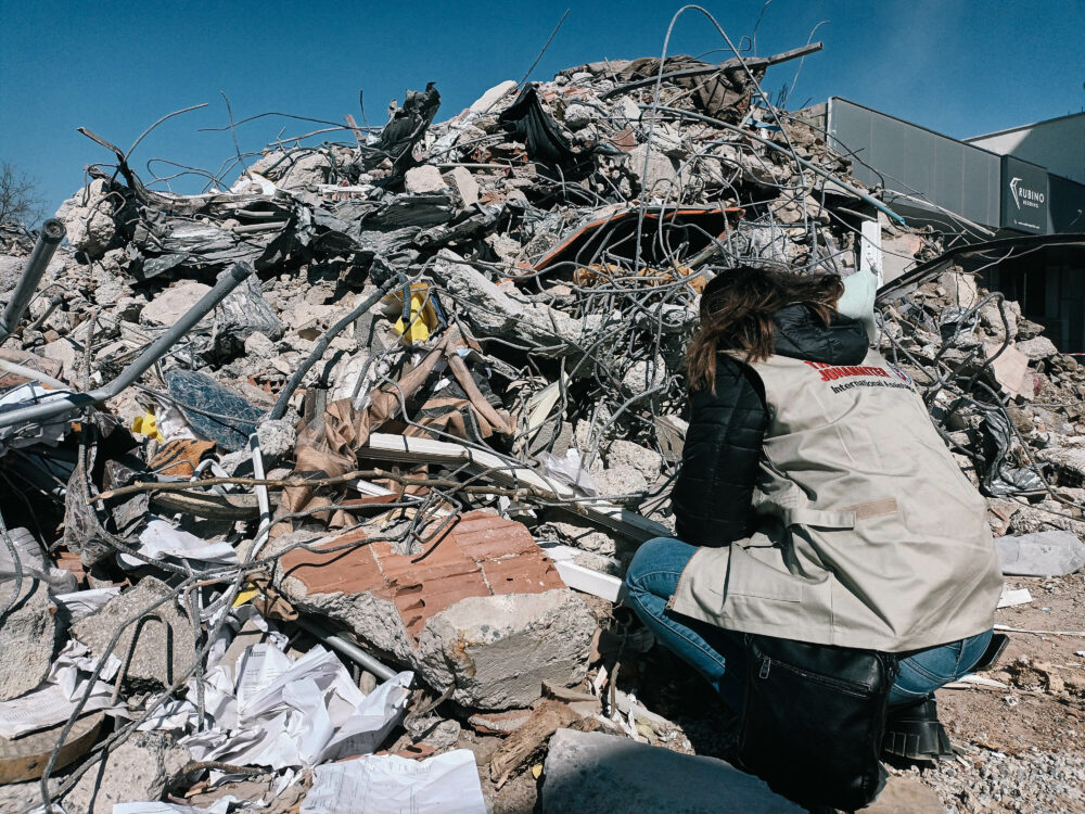 Eine Helferin der Johanniter kniet vor einem Berg aus Trümmern.
