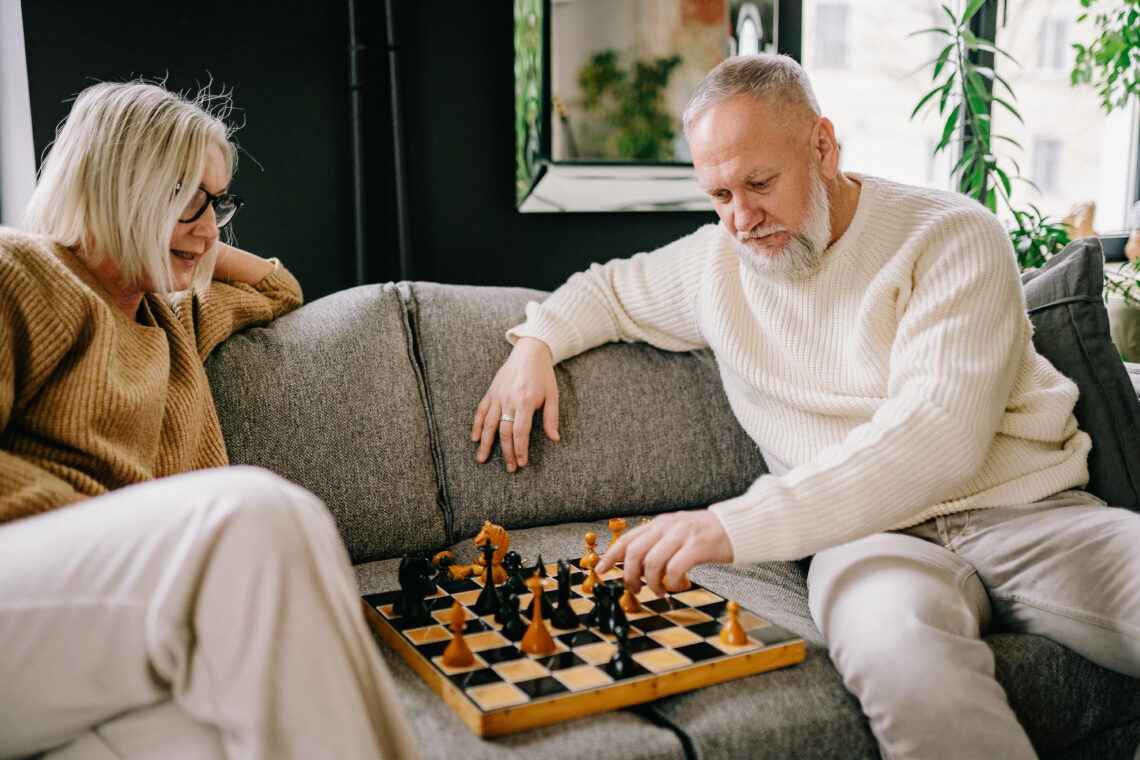 Älterer Mann spielt mit älterer Dme auf einem Sofa Schach