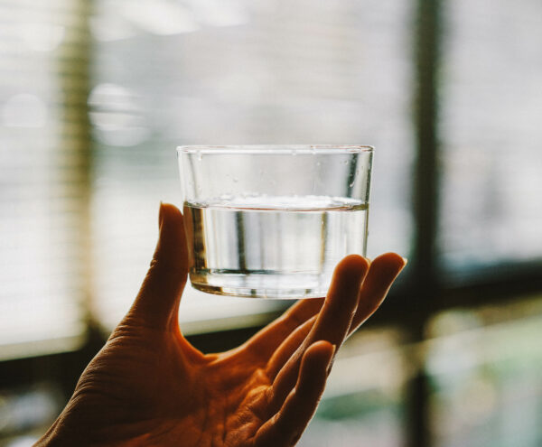 Eine Hand hält ein gefülltes Wasserglas.