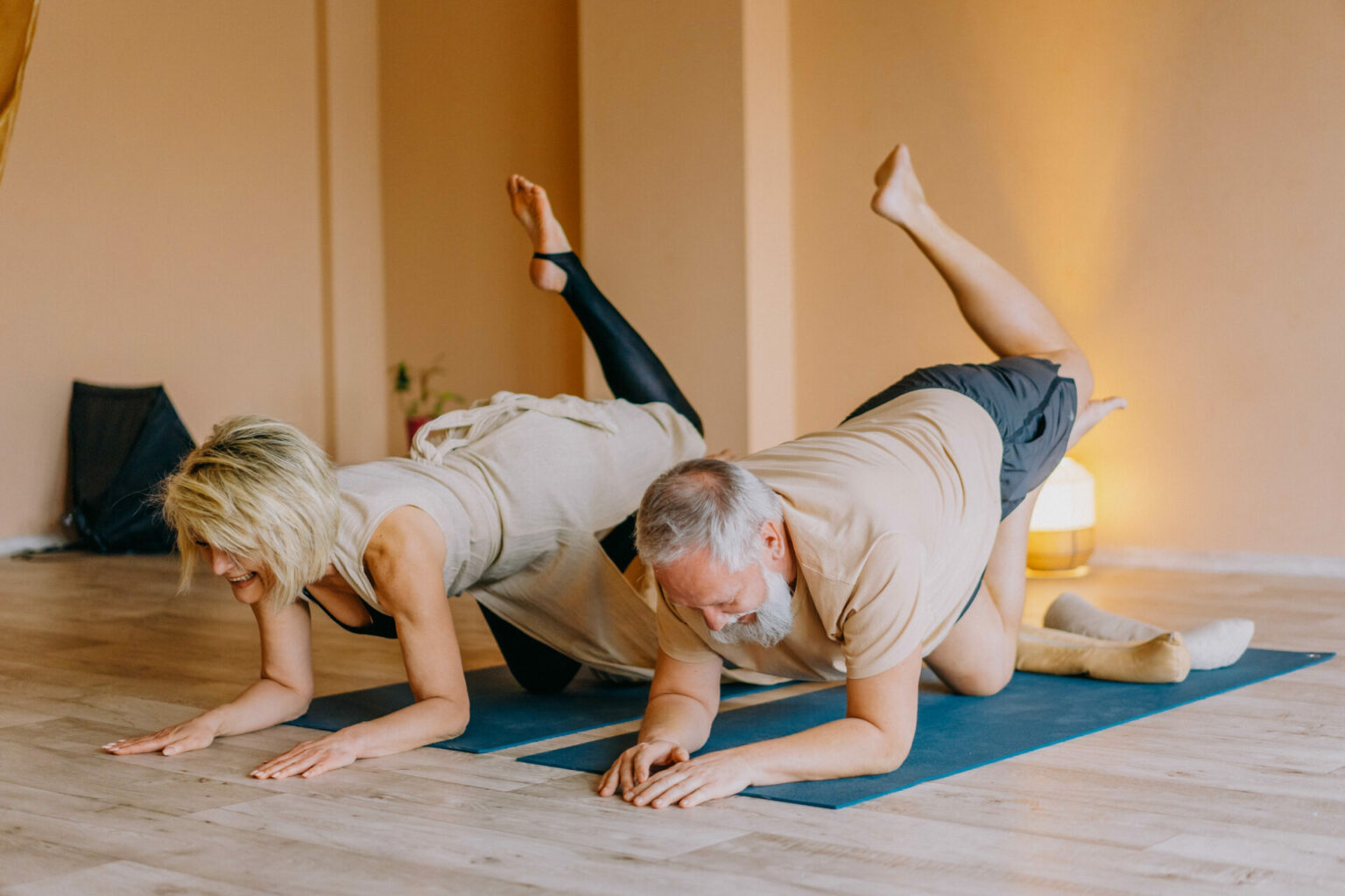 Zwei ältere Menschen auf Yogamatten mit Bein in der Luft.